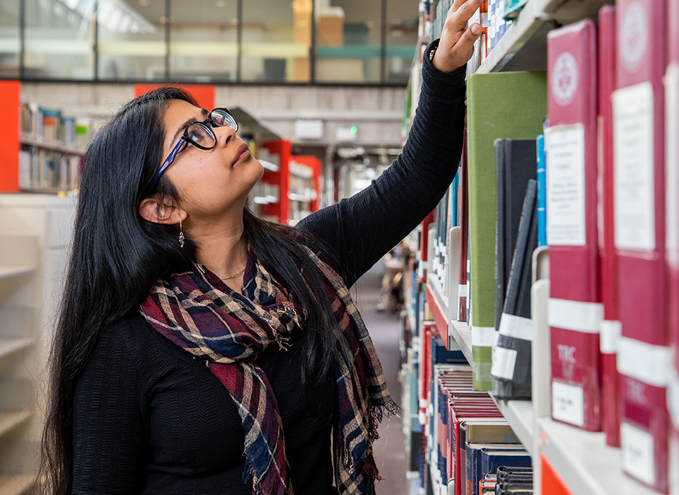 Female student reaching for book on shelf